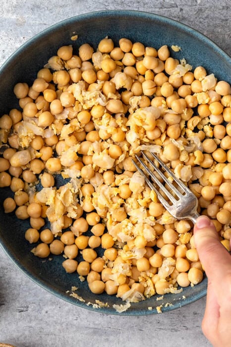 A fork mashing chickpeas in a bowl