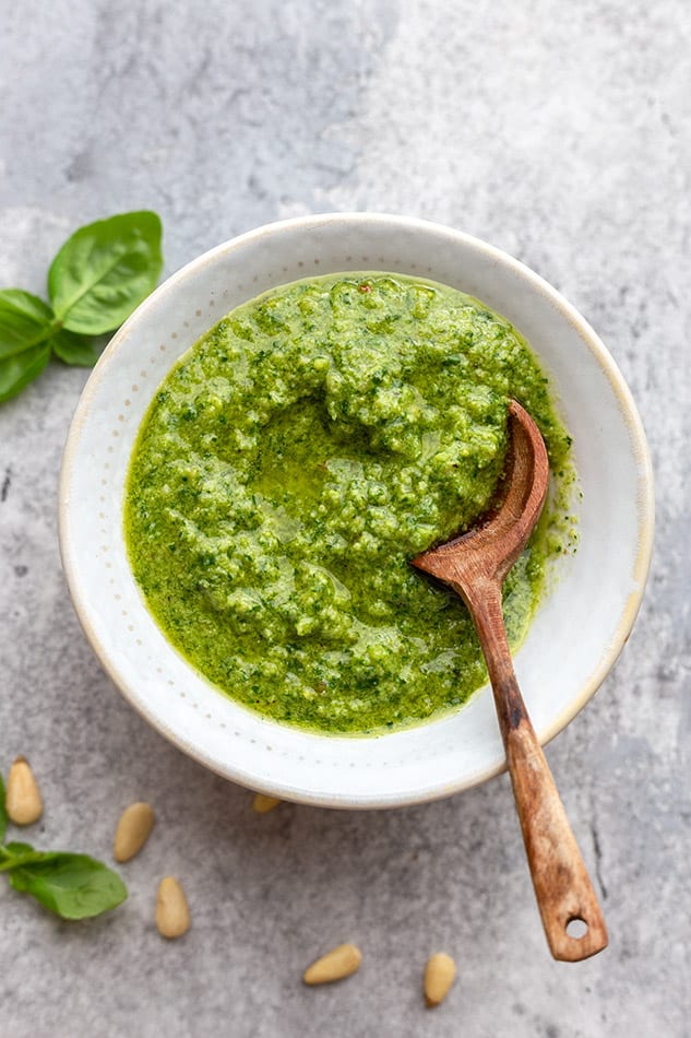 Image of green pesto in white bowl with wooden spoon.