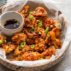 Side shot of a batch of crispy Asian Vegan Cauliflower wings served a savory dipping sauce in a white bowl