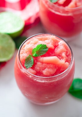 A Watermelon Slushie in a Glass with Fresh Lime Slices in the Background