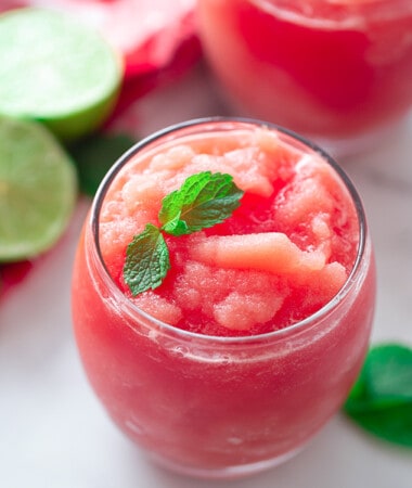 A Watermelon Slushie in a Glass with Fresh Lime Slices in the Background