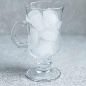 Image of clear glass filled with ice cubes on grey surface.