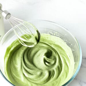 Top view of whipped matcha in a clear bowl with a whisk