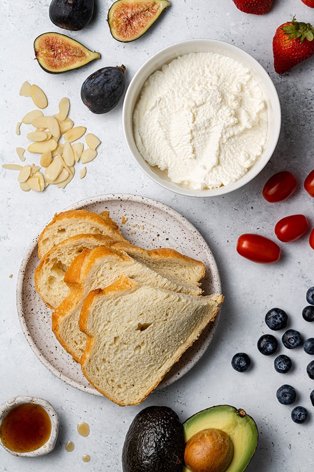 Sliced gluten-free bread, a bowl of whipped ricotta and various toppings laid out on a countertop