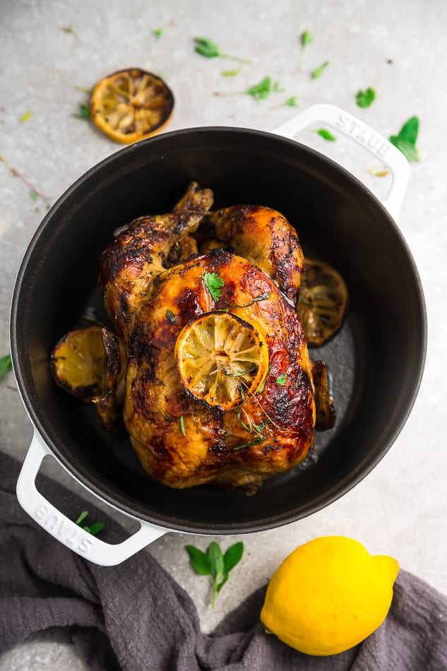 Top view of whole roast chicken with lemon in a white cast iron dutch oven
