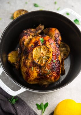 Top view of healthy whole roast chicken with lemon in a white cast iron dutch oven