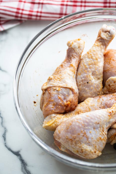 Six raw chicken drumsticks in clear mixing bowl