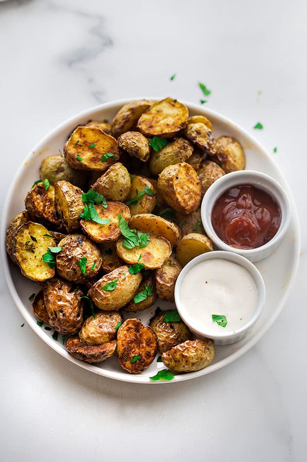 A plate of crispy Air Fryer roasted potatoes beside two small dishes of ketchup and ranch