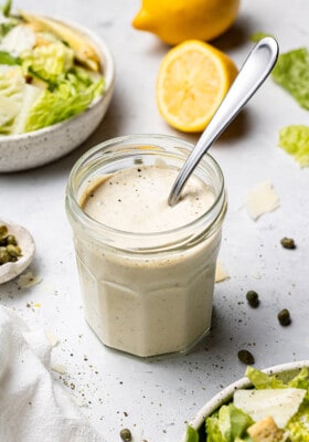 Side view of Vegan Caesar Dressing in a small jar with a spoon