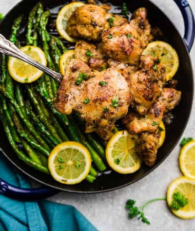 Three crispy air fryer chicken thighs in a blue pan with a side of asparagus