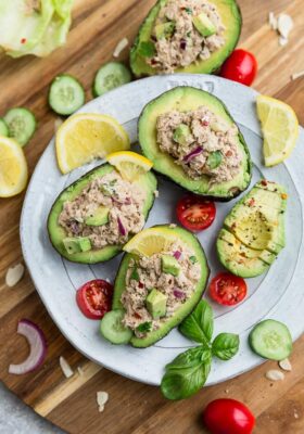 Top view of avocado tuna salad stuffed into 3 avocados on a white plate on a wooden board