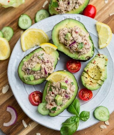 Top view of avocado tuna salad stuffed into 3 avocados on a white plate on a wooden board