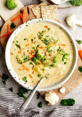 Top view of keto broccoli soup in a white bowl with a spoon on a wooden cutting board