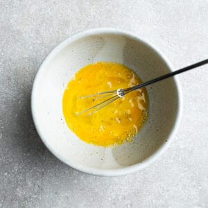 Top view of scrambled eggs in a white bowl with a whisk