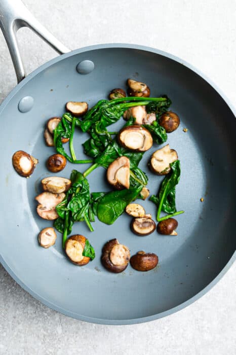 Top view of spinach and mushrooms on a grey nonstick skillet