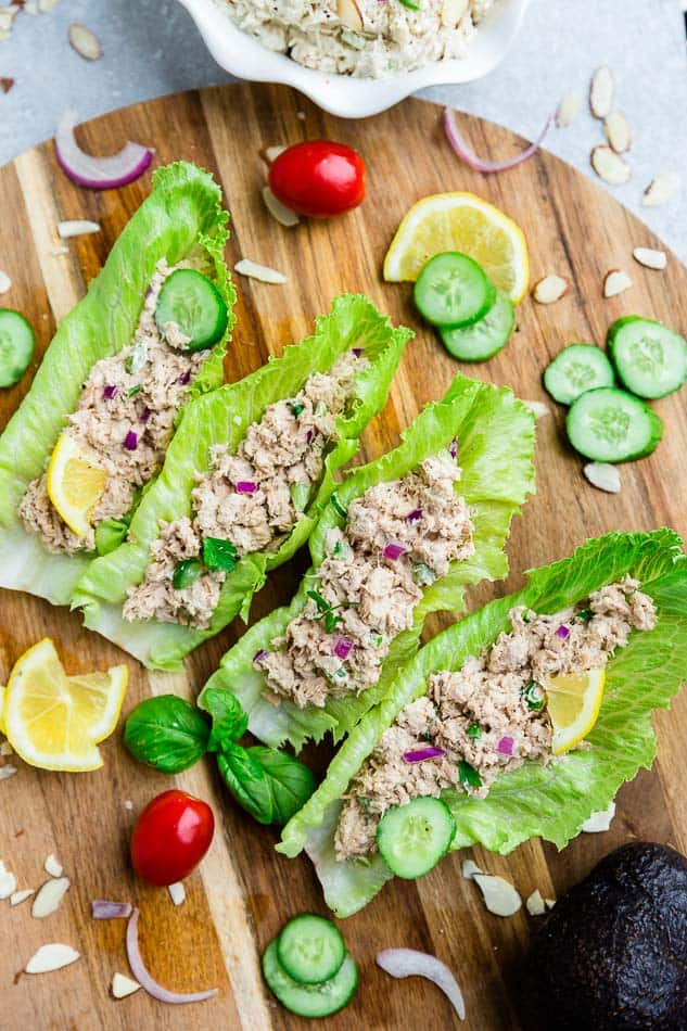 Four lettuce wraps filled with tuna salad on a wooden cutting board