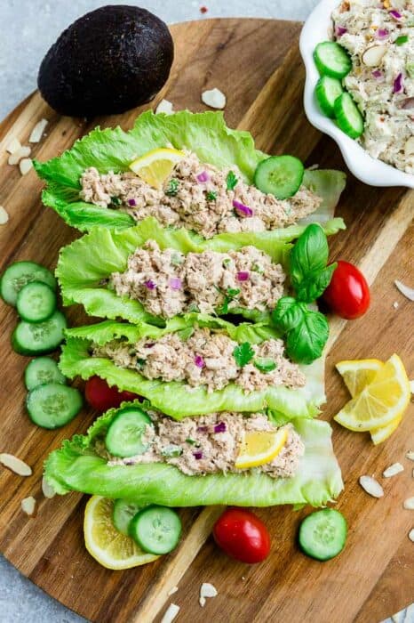 Four tuna salad lettuce wraps lined up on a round cutting board