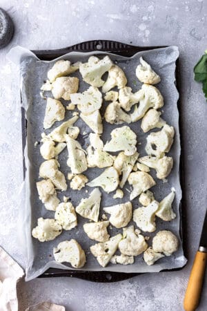 Raw cauliflower florets spread in an even layer on a parchment-lined baking sheet