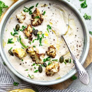 Top view of creamy cauliflower soup in a white bowl with a spoon on a grey background