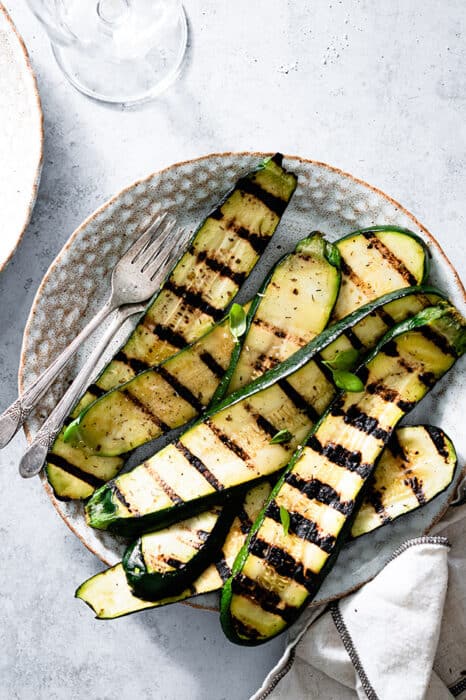 Top view of grilled zucchini slices on white plate with two forks.