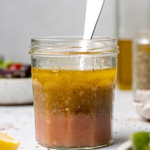 Side view of Italian dressing in a small jar with a spoon