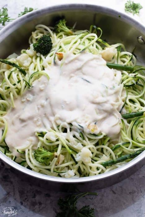 Alfredo sauce on top of Zoodles with cauliflower and broccoli in a skillet