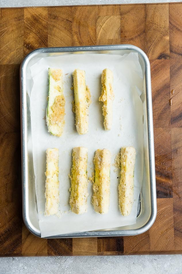 Seven breaded zucchini pieces on a baking sheet lined with parchment paper