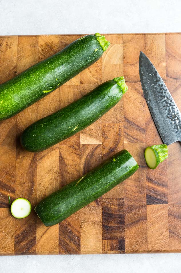 Three medium-sized zucchini on a cutting board with the ends chopped off of one of them