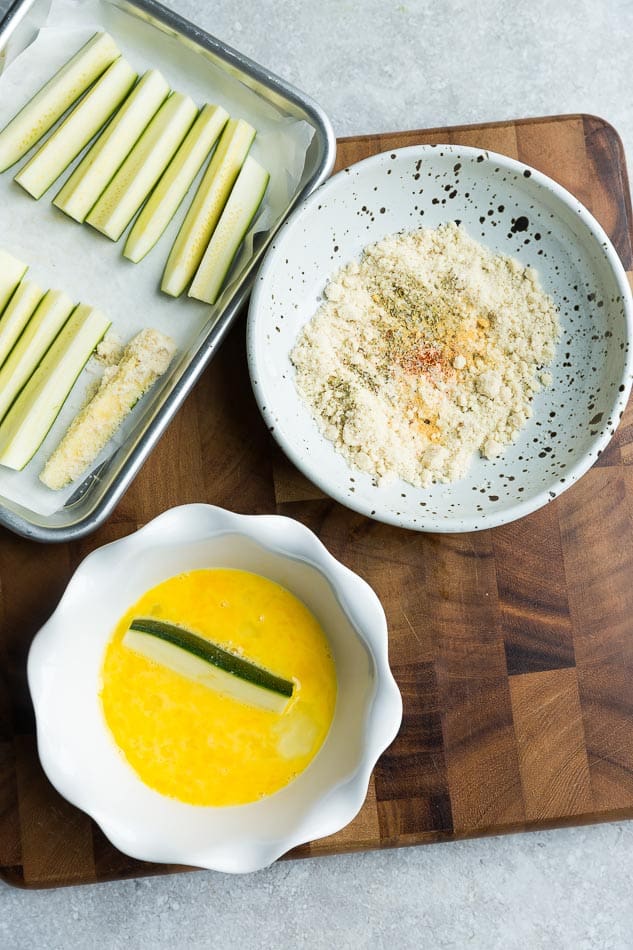 Top view of zucchini slices with egg yolk and breading on wooden cutting board. 