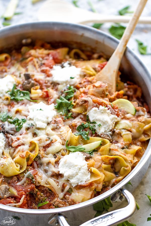 A pot of skillet lasagna topped with ricotta, parsley, and basil, with a wooden spoon sticking out of it 