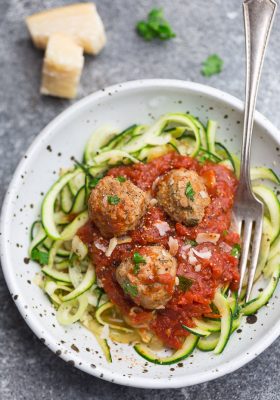 Top view of a bowl of zucchini noodles with tomato sauce and meatballs in a white bowl with a fork