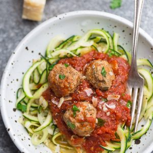Top view of a bowl of zucchini noodles with tomato sauce and meatballs in a white bowl with a fork