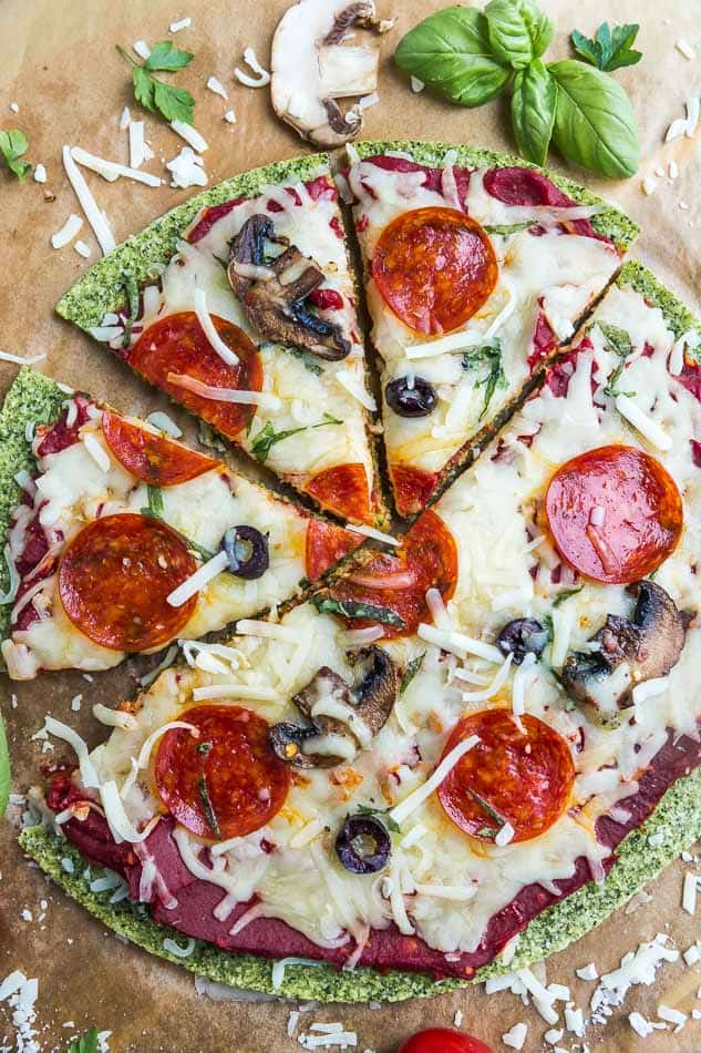 Close-up top view of sliced baked zucchini Pizza Crust with tomato sauce, cheese, mushrooms, olives and pepperoni on brown parchment paper on a baking sheet