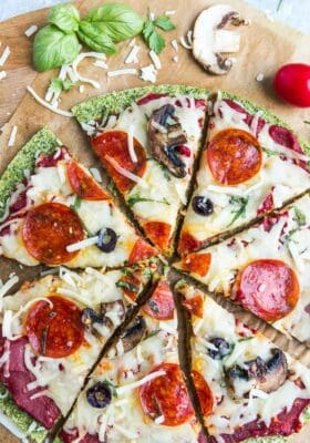 Top view of sliced baked zucchini Pizza Crust with tomato sauce, cheese, mushrooms, olives and pepperoni on brown parchment paper on a baking sheet