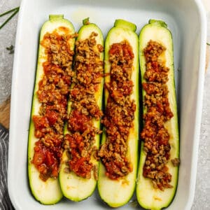 Top view of raw zucchini boats with cooked turkey taco filling in a white casserole dish