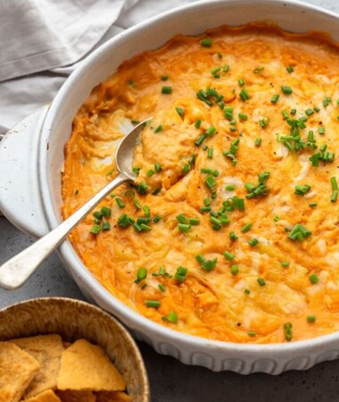 45 degree shot of a batch of vegan buffalo chicken dip in a white round baking dish with a spoon