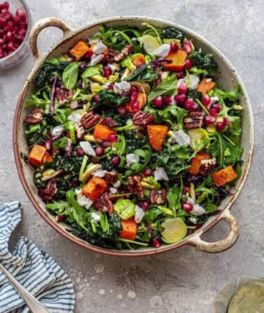 Overhead view of Christmas salad with massaged kale, arugula, Brussels sprouts, roasted sweet potatoe chunks and pomegranate seeds in a round serving bowl.