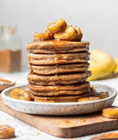 A stack of six banana pancakes topped with caramelized bananas and pure maple syrup
