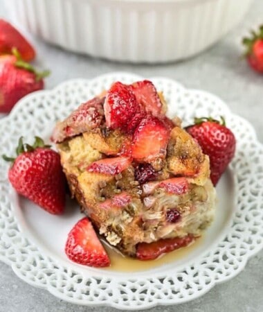 Sideshot of a square of a baked Strawberry French Toast Casserole in a white plate with maple syrup