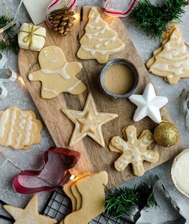 Top view of decorated vegan sugar cookies on a wooden cutting board on a grey background with cookie cutters