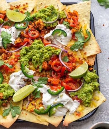 Close-up shot of loaded vegan nachos with guacamole, vegan sour cream and fresh tomato salsa
