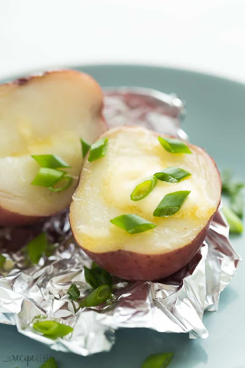 Two halves of an Instant Pot Baked Potato on foil with butter and scallions