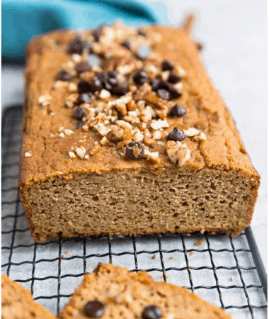 Pumpkin bread with chocolate chips and nuts on top on a cooling rack with a couple slices cut