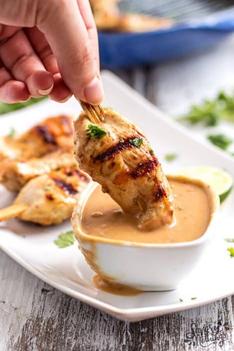 Chicken satay being dipped into peanut sauce