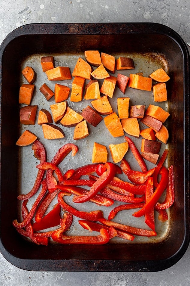 Cubed sweet potatoes and thinly sliced red bell peppers on a baking sheet