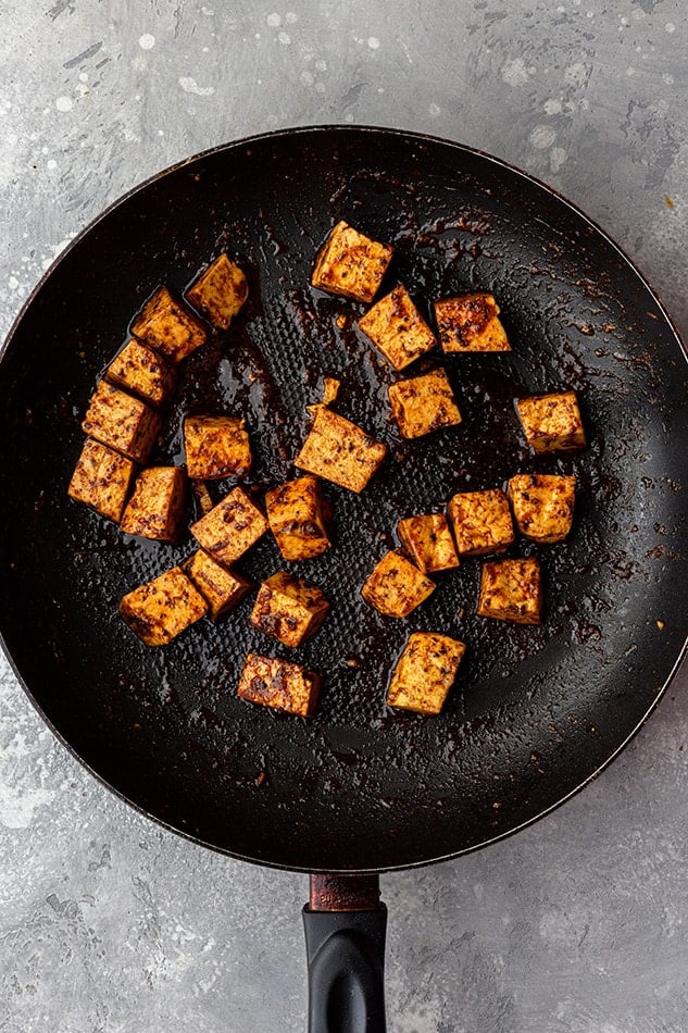 Pan-fried cubes of tofu flavored with taco seasoning inside of a cast-iron skillet